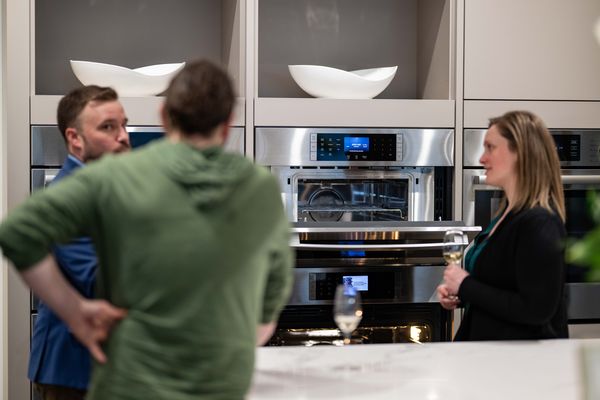 Group of people discussing kitchen appliances in a modern kitchen setting.