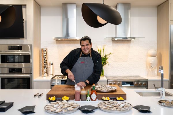 Chef preparing oysters with sauces in a modern kitchen setting.  