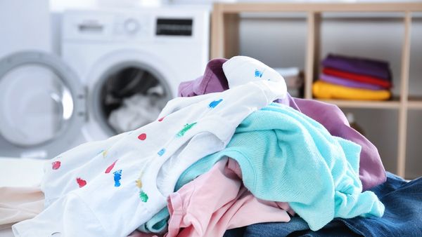 Pila di vestiti colorati su un tavolo davanti a una lavatrice aperta