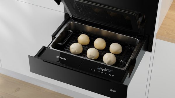       Ein Bosch-Gerät mit einer offenen Schublade, die sechs Teigkugeln auf einem Grill präsentier