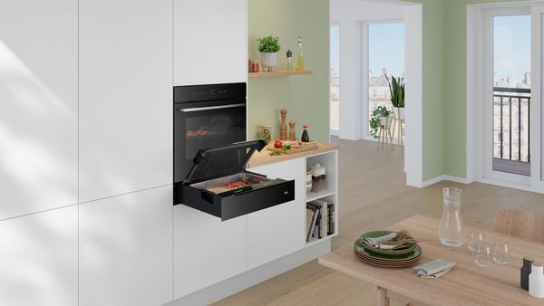       Eine moderne Küche mit einem eleganten schwarzen Ofen und einer offenen Schublade voller frischer Gemüse.     