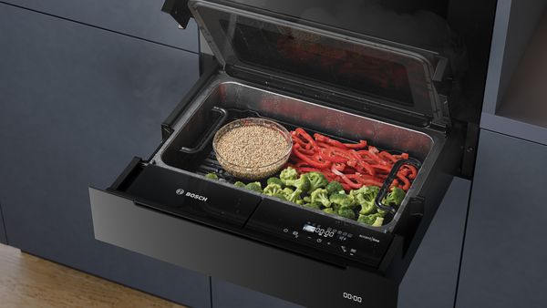 in Bosch Dampfgarer gefüllt mit gedämpftem Brokkoli, rotem Paprika und einer Schüssel Quinoa.