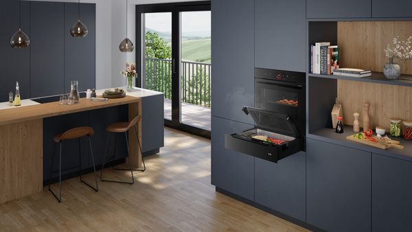 Модерната кухня с тъмни шкафове, дървен остров и отворена фурна с храна вътре.