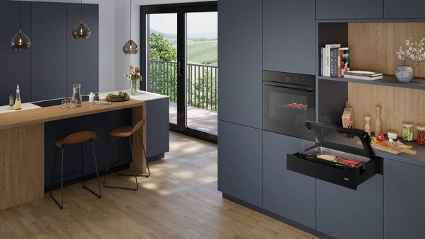 Moderne Küche mit blaugrauen Schränken, Holzakzenten und einem geöffneten Dampfgarer mit Gemüse.