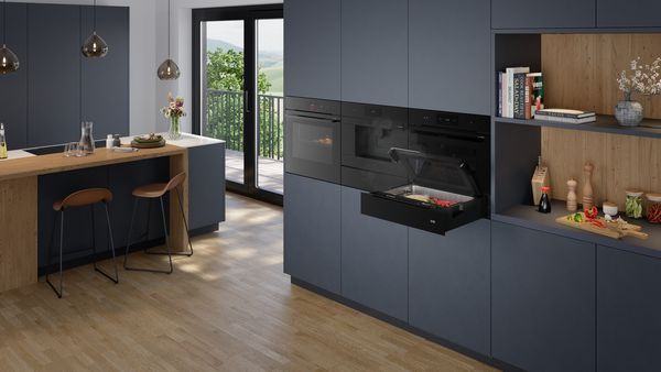 Модерна кухня с вградени готварски уреди, кухненски остров и отворени рафтове с готварски книги.