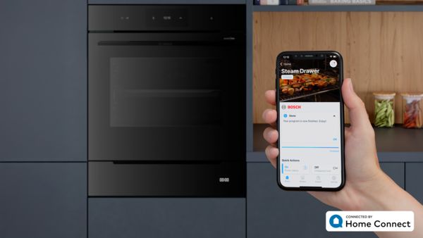 Smarter Dampfgarer und Backofen werden vom Smartphone via Home Connect App bedient. Auf dem Handy-Display ist die Programmabschlussbenachrichtigung zu sehen.