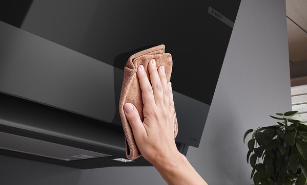 
       Close-up van hand die de hoek van de Bosch Matt Design schuine afzuigkap aanraakt.
      