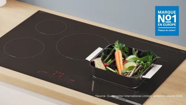 Une poêle contenant des légumes posée sur une table de cuisson à induction.