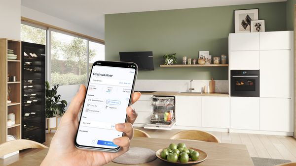 En smartphone med Bosch-appen viser ekspertråd til opvaskemaskinen i baggrunden.
