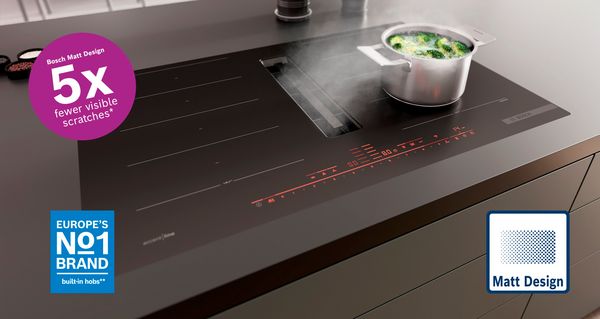1.	Bosch kookplaat met matzwart oppervlak en ingebouwde dampkap. Op de kookplaat staat een dampende kookpot met broccoli.