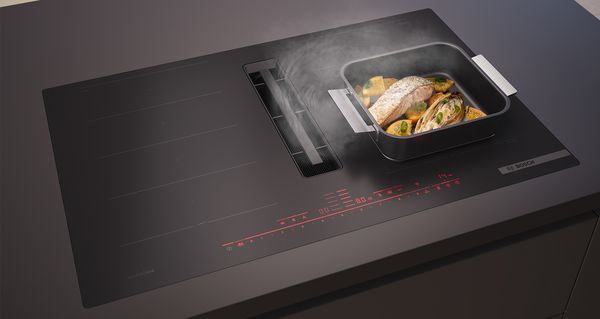 Stijlvolle inductieplaat van Bosch met koolzwarte matte afwerking. Op de kookplaat staat een braadslede met zalm.