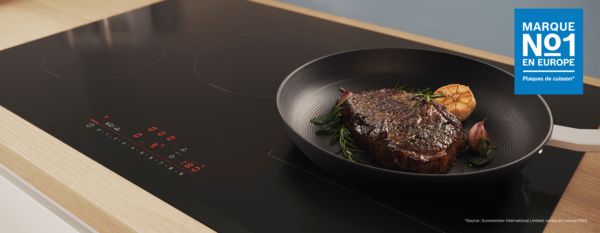 Un steak grillé avec des herbes et de l'ail cuit dans une poêle sur une plaque à induction noire.