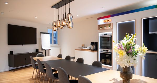 Geräumiges, modernes Esszimmer mit Holztisch, grauen Stühlen, Fernseher und Pendelleuchte.