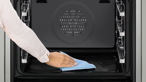 A person's hand wiping the interior of a Bosch pyrolytic self-cleaning oven with a blue cloth, showcasing the cleaning process.
