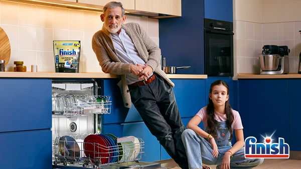 Adult and child in kitchen next to open Dishwasher with Finish pack on top