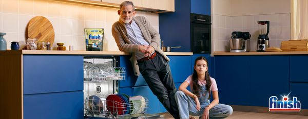 Mu&scaron;karac i žena u kuhinji sa ma&scaron;inom za pranje sudova, kuhinjskim aparatima i plavim ormarićima.