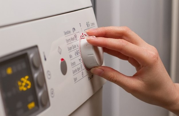 A hand turning the program selection dial on a washing machine.