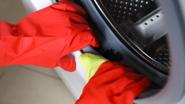 A person wearing red gloves cleans or inspects the rubber door seal of a washing machine. 