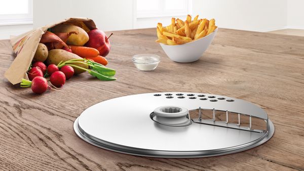 Pommes-Scheibe für Bosch Cookit Küchenmaschine mit Kochfunktion, Zubehör zum Schneiden von Kartoffeln für knusprige Pommes, dargestellt auf Küchenplatte mit Gemüse und Pommes-Schale.