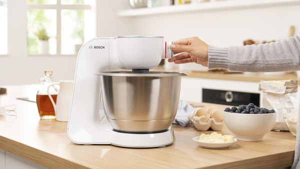 Person verwendet eine Bosch-Küchenmaschine in der Küche, mit Zutaten wie Blaubeeren und Butter in der Nähe.