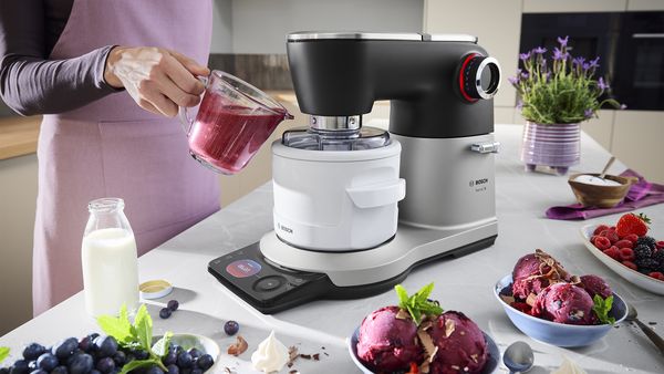 Die Eismaschine der Küchenmaschine Serie 8 ist mit Beerensaft gefüllt. Daneben stehen Schalen mit Eis, Milch und frischen Beeren.