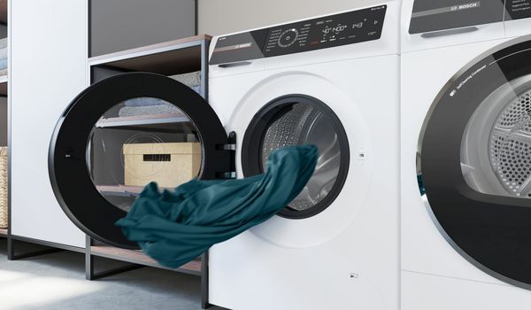 Frontlader-Waschmaschine mit ge&ouml;ffneter T&uuml;r: ein gr&uuml;nes St&uuml;ck Stoff ist in der Trommel sichtbar.