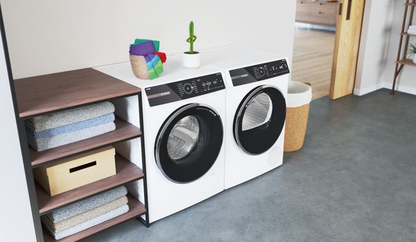 Waschraum mit einer wei&szlig;en Waschmaschine und einem wei&szlig;en Trockner, Holzregalen, gefalteten Handt&uuml;chern und einem Korb.