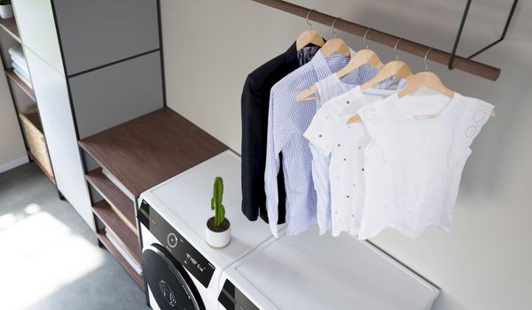 Waschraum mit Waschmaschine, Regal, aufgeh&auml;ngten Kleidungsst&uuml;cken und einem kleinen Kaktus auf dem Ger&auml;t.