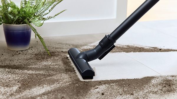 Four different vacuum cleaners are lined up in a bright hallway.