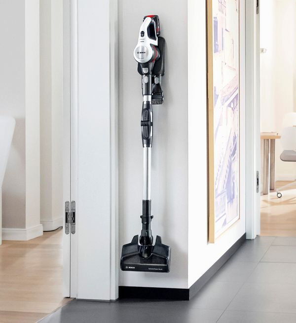 Woman vacuuming up dirt along the edge of the kitchen cabinet with the Unlimited.