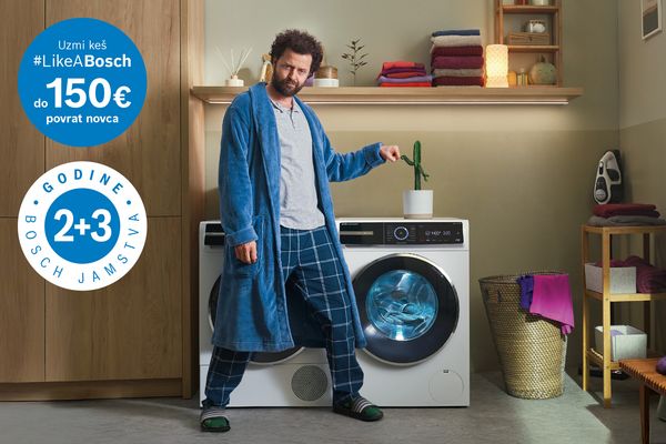 Čovjek u plavom ogrtaču stoji pored perilice rublja, police s ručnicima, interijer doma.