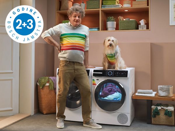 Čovjek stoji pokraj Bosch sušilice rublja, na sušilici sjedi pas, oboje imaju na sebi majice s oznakom energetskog razreda.