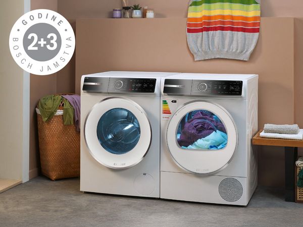 Moderni Bosch perilica i sušilica u stiliziranoj praonici sa šarenom odjećom i oznakom jamstva 2+3 godine