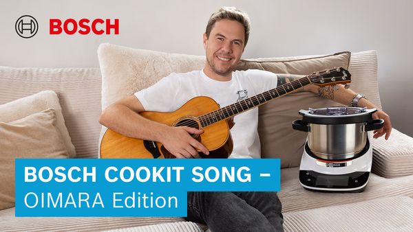 Eine Person sitzt auf einem Sofa und spielt Gitarre neben einem Bosch Kochgerät und wirbt für den Cookit Song - OIMARA Edition.
