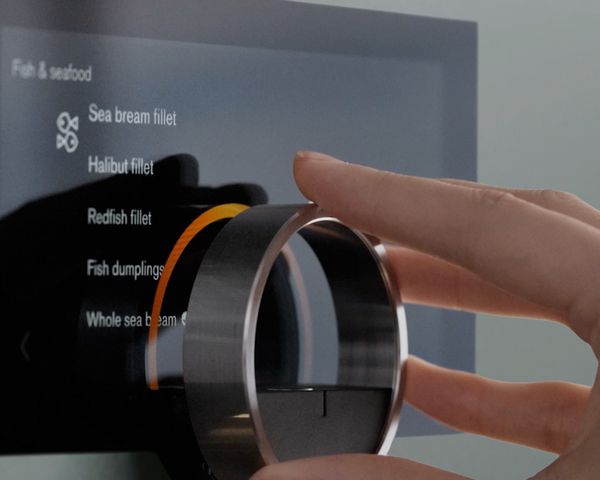 A hand turns the floating control ring on a Gaggenau Minimalistic oven in a Sterling finish