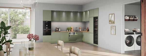 Eine moderne Küche mit grünen Schränken, Holzarbeitsplatten und Geräten, angrenzend an einen Waschbereich.