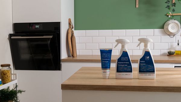 Bosch built-in oven on the left and cleaning and care products in the foreground placed on a kitchen island