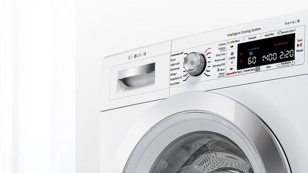 A bottle of liquid detergent pouring blue liquid into the dispenser drawer of a white Bosch washing machine with a control panel and round door