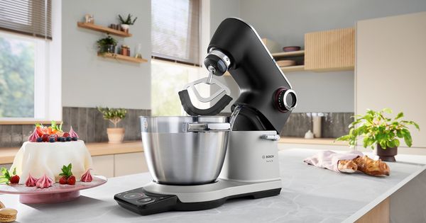Bosch-Küchenmaschine auf der Küchenarbeitsplatte mit Rührschüssel, Kuchen und Gebäck in der Nähe.