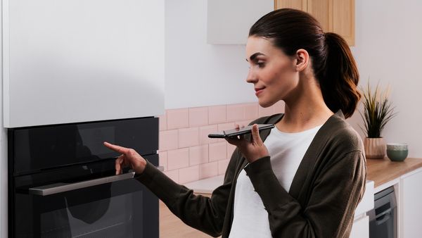 Жена в модерна кухня, използваща гласово управление от смартфон за дистанционно отстраняване на неизправности.