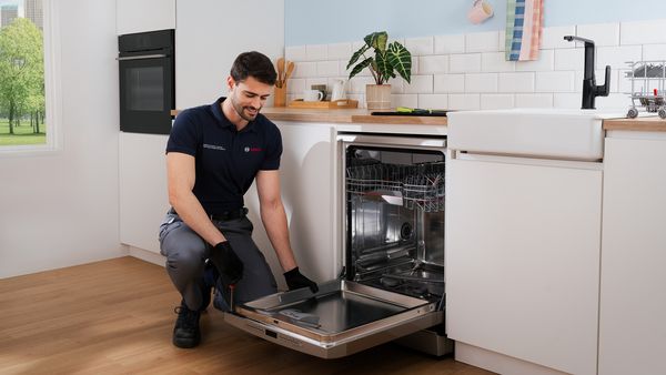 Техник на Bosch ремонтира съдомиялна машина в модерна кухня.