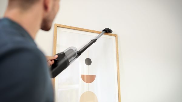 Uomo che utilizza un aspirapolvere Bosch Unlimited con bocchetta per pulire la parte superiore di un quadro appeso al muro