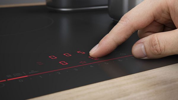 Gros plan du panneau de commande tactile de la plaque de cuisson &agrave; ventilation de la s&eacute;rie 8 au design mat noir carbone. Un doigt appuie sur le panneau de commande tactile.