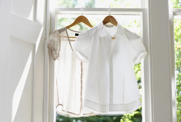 2 חולצות מכופתרות תלויות על קולב על אדן החלון