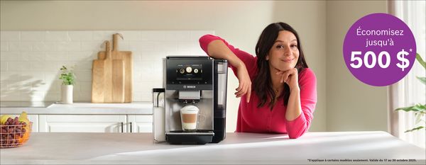 Une femme en pull rose s'appuie sur un comptoir, présentant une machine à café Bosch avec un latte préparé. Une étiquette promotionnelle indique : « Économisez jusqu'à 500 $.