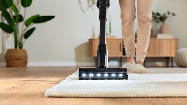 Blick von vorne auf die Düse eines Unlimited Akku-Staubsaugers, mit dem eine Frau einen hellen Teppich absaugt.