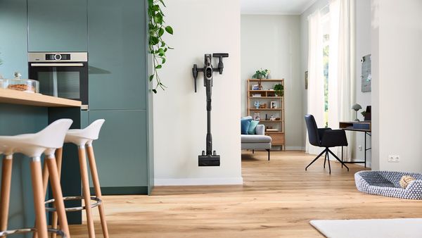 Blick in den Durchgang einer modernen Wohnküche zum Wohnzimmer. An der Wand neben dem Durchgang hängt ein Unlimited 10 Akku-Staubsauger von Bosch in seiner Wandhalterung.