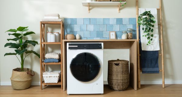 Zona lavanderia con lavatrice Bosch, mensole in legno, piastrelle azzurre e piante decorative.