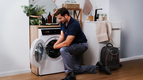 Tecnico inginocchiato davanti all’oblò aperto di una lavatrice Bosch, con una borsa degli attrezzi accanto.