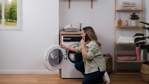 Donna inginocchiata davanti a una lavatrice Bosch con oblò aperto mentre parla al telefono.